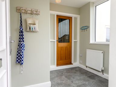 An entryway with a wooden door a radiator a window and hooks on the wall holding an apron and a cloth at Island View in Amble