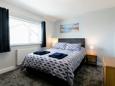 A bedroom with a bed with fish patterned bedding two nightstands with lamps curtains and a painting above the bed at Island View in Amble