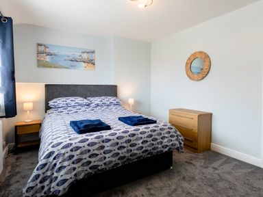 A bedroom with a double bed with fish patterned bedding two bedside tables with lamps a wooden chest of drawers and a round mirror on the wall at Island View in Amble