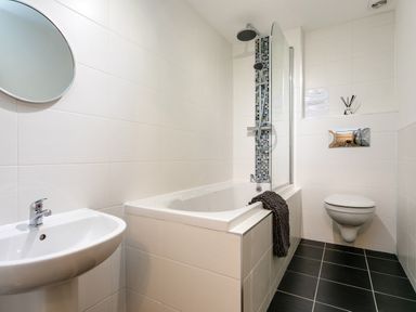 A bathroom with a sink a bathtub with shower and a wall-mounted toilet at Island View in Amble