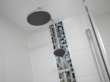 A showerhead and handheld shower fixture mounted on tiled shower wall with a vertical strip of mosaic tiles at Island View in Amble