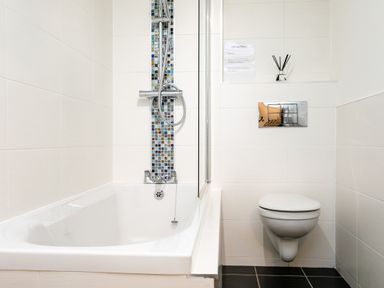 A bathroom with a bathtub and shower next to a wall-mounted toilet at Island View in Amble