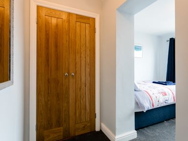 A wooden double door closet next to an open doorway leading to a bedroom with a bed and curtains at Island View in Amble