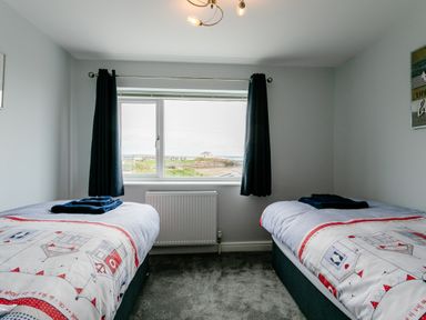 A bedroom with two single beds with patterned bedding and dark curtains at Island View in Amble
