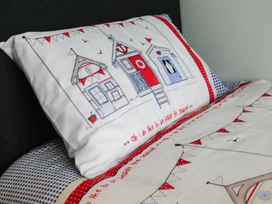 A close up of a pillow and bedding with drawings of beach huts and bunting at Island View in Amble