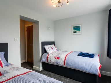 A bedroom with two single beds with patterned bedding a wooden door and a framed seaside picture on the wall at Island View in Amble