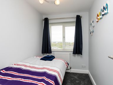 A small bedroom with a bed covered in a striped duvet and folded towels on top with dark curtains and a window at Island View in Amble