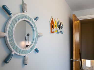 A wall with a nautical ship wheel mirror and colorful house-shaped hooks next to a partially open wooden door at Island View in Amble