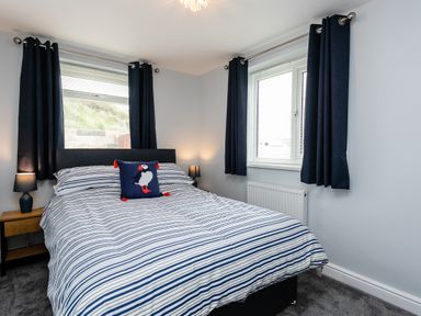 A bedroom with a bed with striped bedding two windows with navy curtains and two bedside tables with lamps at Island View in Amble