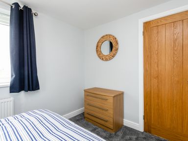 A bedroom corner with a wooden chest of drawers a round mirror above a wooden door and a window with dark curtains at Island View in Amble