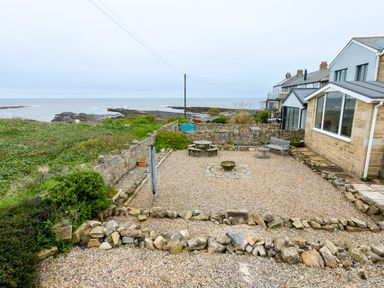 A gravel yard with outdoor seating and stone walls overlooking a rocky coastline at Island View in Amble