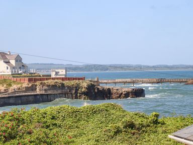A coastal scene with a pier extending over the water and buildings on cliffs at Island View in Amble