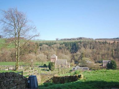 A rural landscape with a church and gravestones surrounded by fields and trees at Kirknowe in Jedburgh