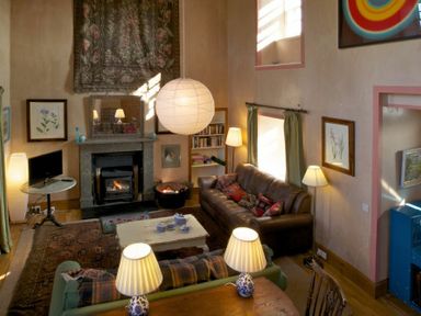 A living room with a fireplace brown sofa green curtains and lamps at Kirknowe in Jedburgh