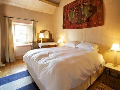 A bedroom with a large bed lamps a wooden dresser with mirror a chair and a window at Kirknowe in Jedburgh