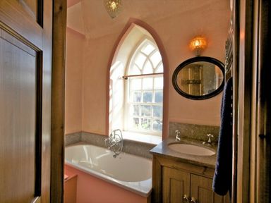 A bathroom with a bathtub under an arched window and a sink with an oval mirror above at Kirknowe in Jedburgh