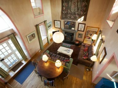 A living room with sofas a fireplace a round wooden table with lamps and green curtains at Kirknowe in Jedburgh