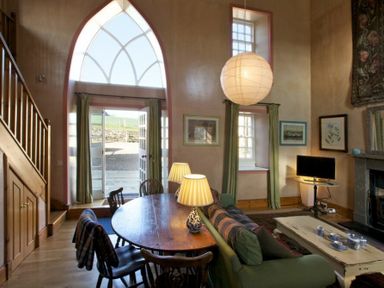 A living room with a round wooden table and chairs a green sofa green curtains a hanging lamp and a TV at Kirknowe in Jedburgh