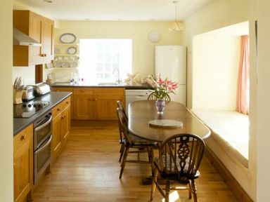 A kitchen with wooden cabinets a table with chairs and flowers on it at Kirknowe in Jedburgh