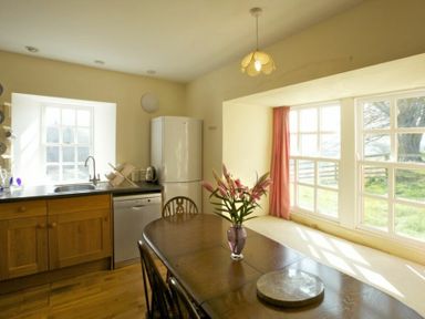 A kitchen with wooden cabinets a refrigerator a dining table with flowers and large windows with pink curtains at Kirknowe in Jedburgh