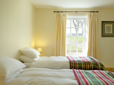 A bedroom with two single beds near a window with curtains and a small bedside lamp at Kirknowe in Jedburgh