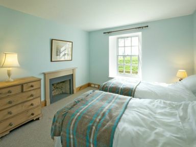 A bedroom with two beds a wooden dresser a lamp a fireplace and a window at Kirknowe in Jedburgh