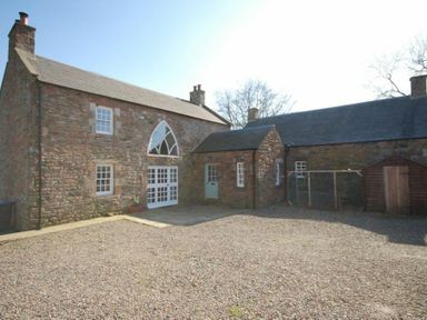 A stone building with multiple windows and doors and a gravel courtyard at Kirknowe in Jedburgh