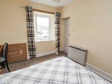 A bedroom with a bed, window, door, and box at Kittiwake Cottage, Budle Bay in Bamburgh