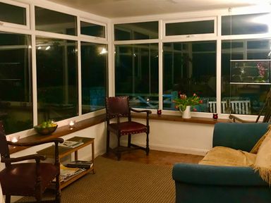 A sitting area with two wooden chairs a small wooden table a blue sofa a vase of flowers and windows at Leazes Cottage in Rothbury