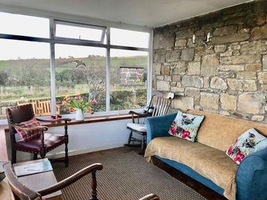 A sitting room with a blue sofa and armchairs next to a large window and stone wall at Leazes Cottage in Rothbury