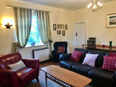 A living room with leather sofas a wooden coffee table curtains on the window and framed butterfly pictures on the wall at Leazes Cottage in Rothbury