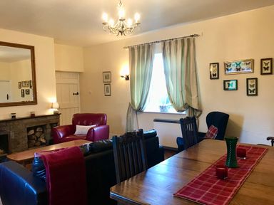 A living room with armchairs a wooden dining table with candles and a vase a fireplace and butterfly pictures on the wall at Leazes Cottage in Rothbury