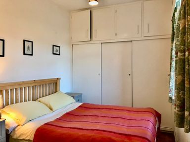 A bedroom with a wooden bed frame red striped bedding and white built in cupboards at Leazes Cottage in Rothbury