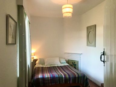A small bedroom with a bed covered in a striped blanket next to a window with curtains and a bedside lamp at Leazes Cottage in Rothbury