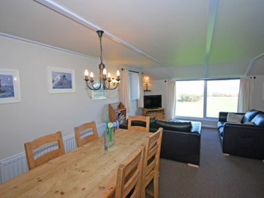 A dining table with wooden chairs and a living room with black sofas and a television near a large window at Longstone in Embleton