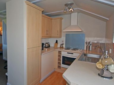 A kitchen with wooden cabinets a white oven stovetop and a sink with cups on the counter at Longstone in Embleton