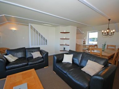 A living room with two black leather sofas pillows on them a wooden coffee table and a dining area with a wooden table and chairs at Longstone in Embleton