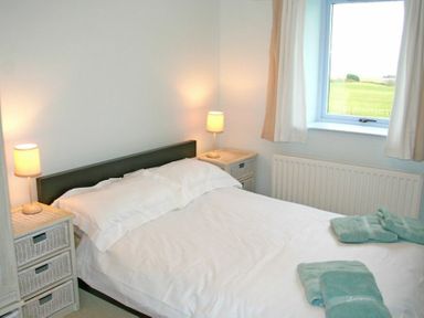 A bedroom with a double bed with white linens two bedside tables with lamps and a window showing a green field at Longstone in Embleton