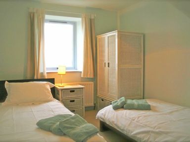 A bedroom with two single beds a bedside table with a lamp a window with curtains and a wardrobe at Longstone in Embleton