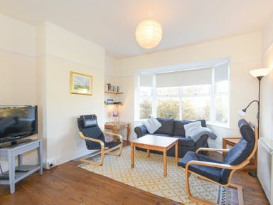 A living room with a sofa two armchairs a wooden coffee table a television on a stand and a large window at Melvin Cottage in Low Newton-By-The-Sea