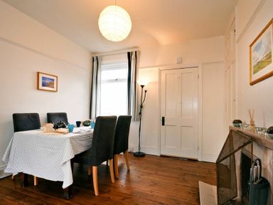 A dining room with a table covered with a cloth set for tea four chairs wooden floor and a fireplace at Melvin Cottage in Low Newton-By-The-Sea