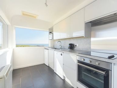A kitchen with white cabinets a stove an oven a sink a kettle and a window with a sea view at Melvin Cottage in Low Newton-By-The-Sea