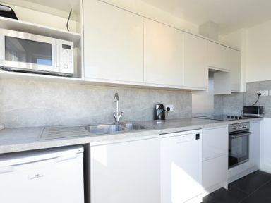 A kitchen with white cabinets a microwave a kettle a toaster a sink and an oven at Melvin Cottage in Low Newton-By-The-Sea
