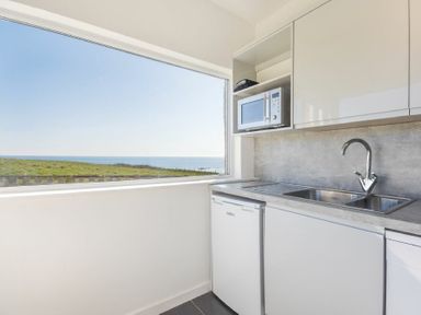 A kitchen with a sink microwave refrigerator and a window view of the sea at Melvin Cottage in Low Newton-By-The-Sea
