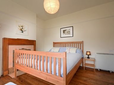 A bedroom with a wooden bed, side table with lamp, fireplace and flower pictures on the walls at Melvin Cottage in Low Newton-By-The-Sea