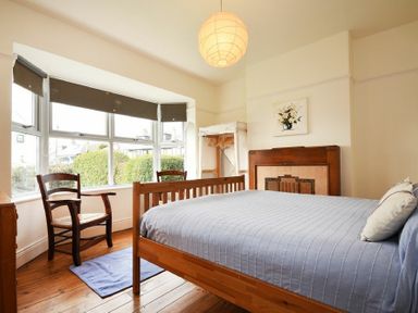 A bedroom with a wooden bed a chair a window with blinds and a fireplace at Melvin Cottage in Low Newton-By-The-Sea