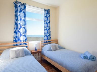 A bedroom with two single beds blue bedding a wooden bedside table and window with blue patterned curtains at Melvin Cottage in Low Newton-By-The-Sea