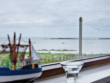 A model ship and a glass on a windowsill overlooking the sea with boats and a concrete pole outside at Melvin Cottage in Low Newton-By-The-Sea