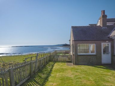 A seaside cottage with a grassy yard and wooden fence overlooking the ocean at Melvin Cottage in Low Newton-By-The-Sea