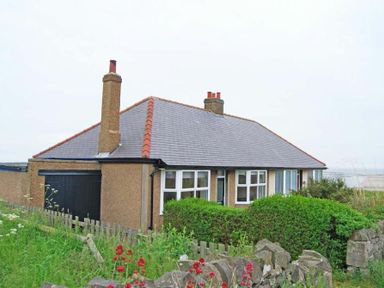 A house with a tiled roof and chimneys surrounded by greenery and a stone wall at Melvin Cottage in Low Newton-By-The-Sea